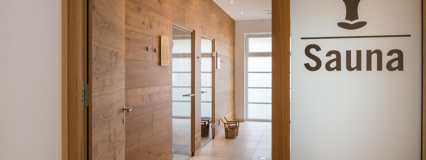 Heller, einladender Saunabereich mit stilvollen Holzwänden und großflächigem Glasdesign im Almhotel Kärnten. Die warme Beleuchtung und die klare Raumgestaltung schaffen eine entspannte Atmosphäre für erholsame Wellnessmomente. Eingang zur Saunawelt des Almhotel Kärnten am Nassfeld