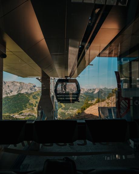 Blick aus der Bergstation der Gartnerkofelbahn auf eine Kabine vor der sommerlichen Alpenkulisse am Nassfeld in Kärnten. Die dunkle Innenansicht rahmt Berge, Seilbahn und sonnige Landschaft stimmungsvoll ein und vermitteln die besondere Atmosphäre eines Kärnten-Urlaubs in den Bergen ganz nahe beim Almhotel Kärnten. Gartnerkofelbahn am Nassfeld im Sommer