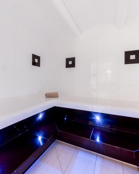 Dieses elegante Dampfbad bietet eine beruhigende Atmosphäre mit weiß glänzenden Wänden, stilvollen LED-Lichtern und komfortablen Sitzflächen. Die moderne Ausstattung sorgt für optimale Entspannung und Wohlfühlmomente im Almhotel Kärnten – perfekt für Ihre Wellness-Auszeit. Modernes Dampfbad mit LED-Beleuchtung in der Saunawelt des Almhotel Kärnten am Nassfeld