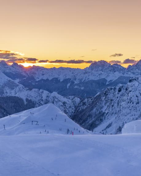 Eine verschneite Alpenlandschaft in Kärnten, eingefangen bei Sonnenuntergang. Die schneebedeckten Berge leuchten im warmen Licht, der glühende Horizont erzeugt eine friedliche und romantische Stimmung. Ideal für Wintersport, Naturgenuss und einzigartige Fotomomente. Winter-Sonnenstimmung am Nassfeld in Kärnten mitten in den Karnischen Alpen