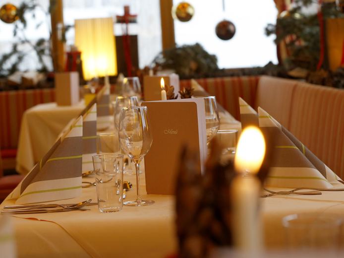 Stimmungsvoll gedeckter Tisch im Restaurant des Almhotel Kärnten mit eleganten Gläsern, Kerzenschein und dekorativen Elementen. Die warme Beleuchtung und liebevolle Dekoration schaffen eine einladende Atmosphäre für ein genussvolles Essen im festlichen Ambiente. Festlich gedeckter Restauranttisch im Almhotel Kärnten am Nassfeld