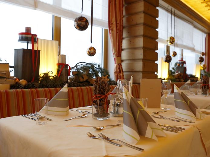 Ein elegant gedeckter Tisch im Almhotel Kärnten, dekoriert mit Stoffservietten, stilvollen Gläsern und winterlichen Akzenten. Warme Beleuchtung und weihnachtliche Dekoration schaffen eine gemütliche, einladende Atmosphäre für unvergessliche Genussmomente im Restaurant. Festlich gedeckter Tisch im Almhotel Kärnten am Nassfeld