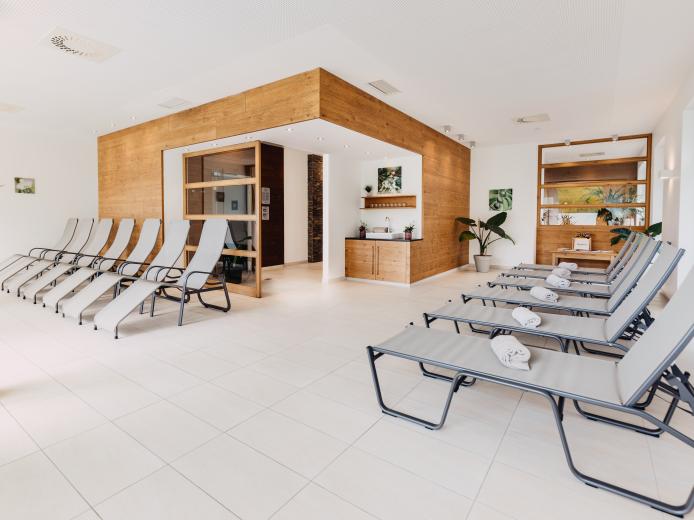 Moderner und heller Ruheraum in der Saunawelt, dem Wellnessbereich mit komfortablen Liegen, sanftem Tageslicht und einer gemütlichen Atmosphäre. Der Raum ist stilvoll eingerichtet mit Holzelementen und Pflanzen, ideal für Entspannung nach Saunabesuchen im Almhotel Kärnten. Ruheraum in der Saunawelt des Almhotel Kärnten am Nassfeld