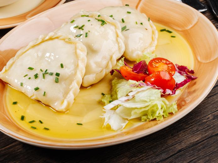 Frisch zubereitete Kärntner Kasnudeln, traditionell mit aromatischer Fülle serviert, mit feiner Buttersauce und frischem Schnittlauch serviert im Almhotel Kärnten am Nassfeld. Hausgemachte Kärntner Kasnudeln im Almhotel Kärnten am Nassfeld